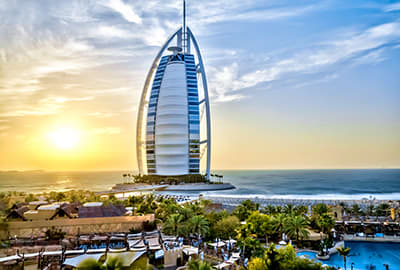 Dubai Visa Burj Al Arab luxury hotel at sunset overlooking Dubai beach and Arabian Gulf with palm trees and resort pool in foreground